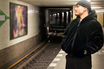 A stylish young man in a black coat waiting at an underground subway platform