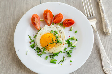Fried eggs with greens and tomatoes on a white plate
