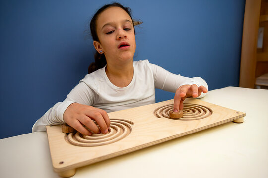 A child practices brain training with a didactic wooden toy, using both hands to enhance cognitive and motor development.