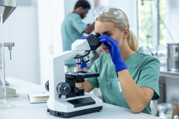 Woman scientist using microscope in laboratory conducting biomedical analysis