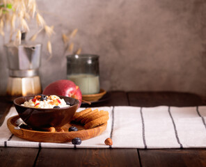 Fresh cottage cheese with blueberries and apple slices in a brown bowl with oatmeal cookies on a dark wooden background. Breakfast concept.