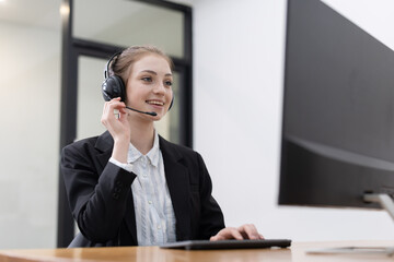 Caucasian woman is engaged in a conversation using a headset while working at a computer