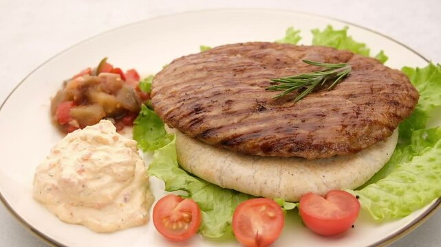 Serbian pljeskavica served with traditional Balkan side dishes. Balkan style burger pljeskavica grilled meat patty on a plate with Serbian salad and sauce