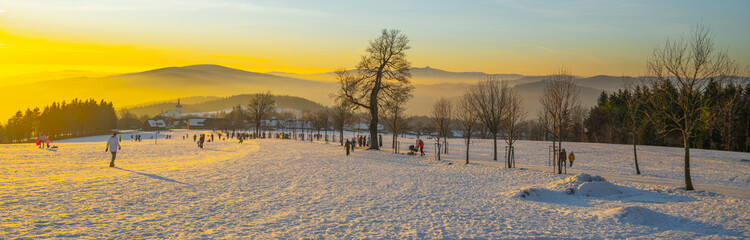 At sunset in Prichovice, Czechia, people enjoy the winter landscape covered in snow. The vibrant...