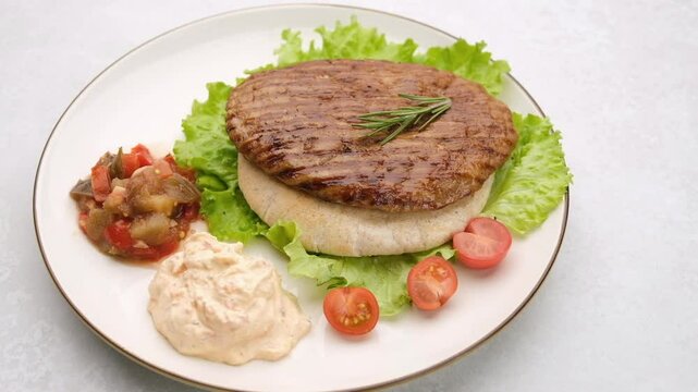 Serbian pljeskavica served with traditional Balkan side dishes. Balkan style burger pljeskavica grilled meat patty on a plate with Serbian salad and sauce. Truck camera movement