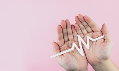 Paper ECG signal in hand on pink background. Concept of health care, atrial fibrillation,...