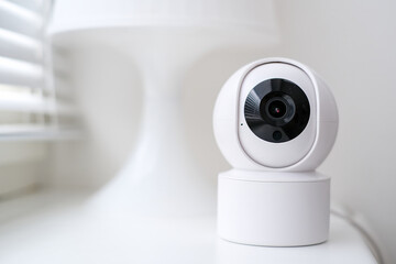 Smart home security camera on a white table near a window.
