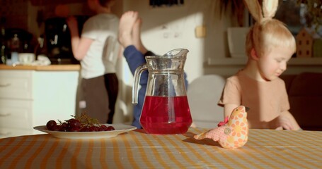 In a cozy kitchen, one child happily enjoys a drink and snack at the table, while another playfully...