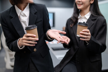 Two businesswomen standing in a group meeting around a table in a modern office. There are documents, laptops. Everyone is brainstorming, planning sales, digital marketing and growth strategies.