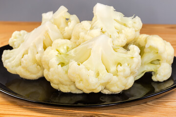 Blanched cauliflower pieces on black plate, front view close-up
