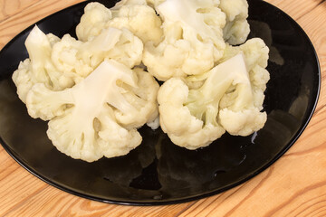 Blanched cauliflower pieces on the black plate on rustic table