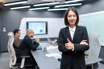 Businesswoman standing poses, group meeting around a table in modern office, documents, laptops and graphs are placed, everyone brainstorming, planning sales, digital marketing and growth strategies.