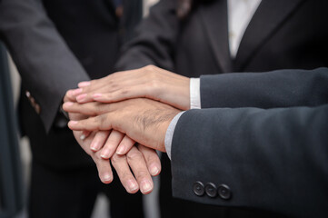 Obraz premium Businessmen and women standing posing together, hands clasped, meeting in office, documents, laptops, sales planning, digital marketing and growth strategies with colorful charts and graphs.