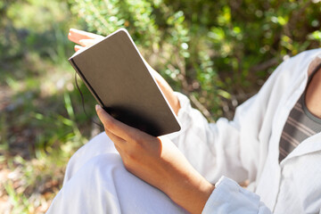 Close-up of hands turning pages of a black notebook outdoors