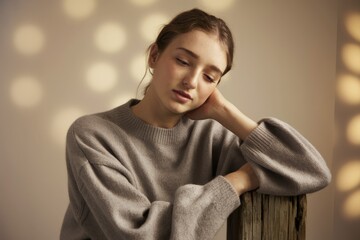Fototapeta premium A pensive young woman in a soft grey sweater, lost in thought, bathed in soft light.