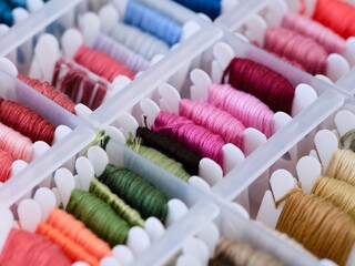 Plastic bobbins with different colour embroidery threads in a plastic sorting box. Close-up