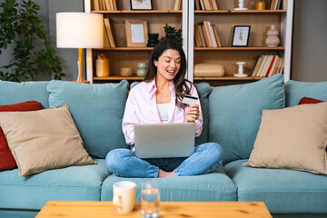 Young smiling happy independent woman sitting at home on sofa, making purchase. Online shopping...