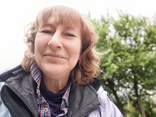 Middle-aged woman enjoys park surroundings while taking selfies during an adventurous travel trip