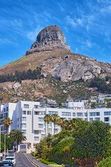 Naklejka premium Mountain, building and road with blue sky of city, landmark or landscape view of urban suburb. Empty, space or big rock with trees, architecture or plants of natural environment, town or residence