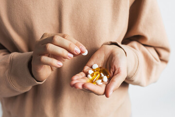 A person in a beige sweater holding various pills and capsules in one hand while picking up a...