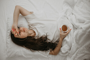 Woman lying in bed with coffee cup, relaxing morning vibes