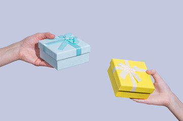Hands holding two gift boxes blue and yellow on a light background.