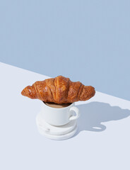 Fresh croissant on a cup of cappuccino or latte coffee on white and blue  background with shadow.