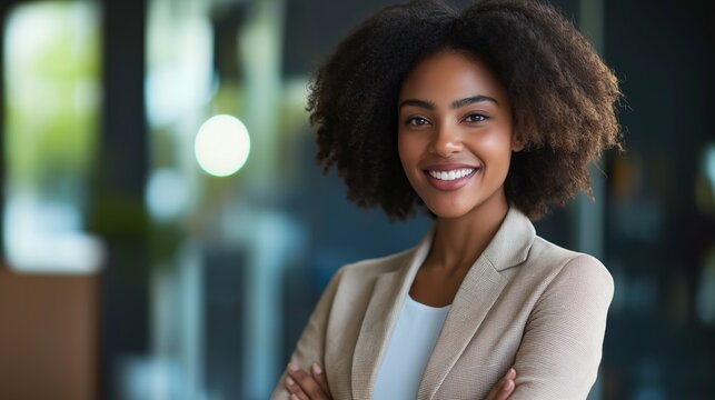 A young african american woman stands confidently in a stylish office environment, displaying a warm smile. The soft light filters through large windows, illuminating her joyful expression