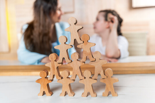 Wooden men are arranged in a pyramid. In the background is a psychologist working with a child. A psychologist sees a little girl in the office. Selected focus