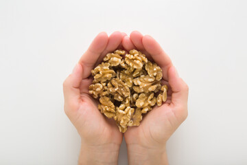 Young adult woman opened palms holding heap of brown walnuts on light gray table background. Closeup. Point of view shot. Top down view.