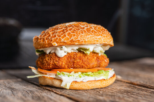 Crispy chicken burger with fresh lettuce, tomato, and a creamy sauce, served in a rustic setting on a wooden table.

