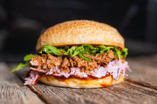 Pulled beef burger with fresh arugula, coleslaw, and barbecue sauce, served on a rustic wooden table.