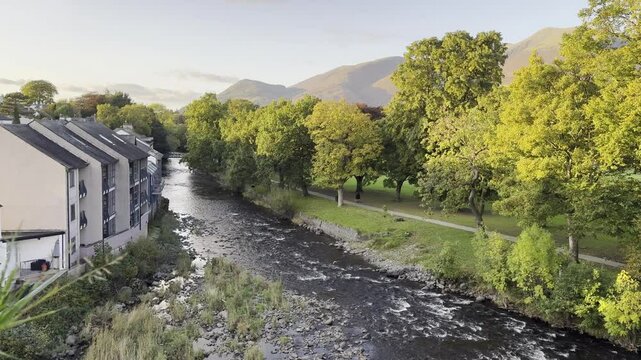 View over Keswick River Greta at golden hour sunset with golden trees and Skiddaw in the background; taken from Keswick YHA