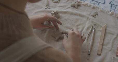 Artist shaping a star from clay using sculpting tools on a linen surface. Detailed closeup of handmade ceramic creation, showcasing pottery techniques and craftsmanship in progress.