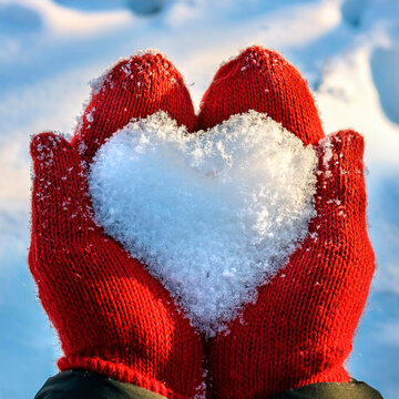 Neve a forma di cuore tenuti in mano da una ragazza con guanti di lana rossa
