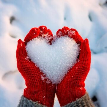 Neve a forma di cuore tenuti in mano da una ragazza con guanti di lana rossa