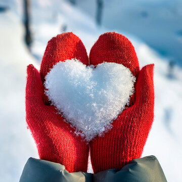 Neve a forma di cuore tenuti in mano da una ragazza con guanti di lana rossa