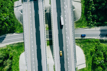 Aerial drone view of highway asphalt road with cars and trucks driving through green summer woods....