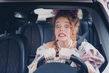 Young woman in elegant vintage dress driving a car with a funny expression, blending past and...