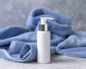 White blank one pump bottle near blue bath towel closeup, mockup. Natural handmade cosmetic