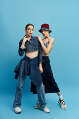 Twins showcase fashion flair in stylish denim and vibrant hats against a bold backdrop