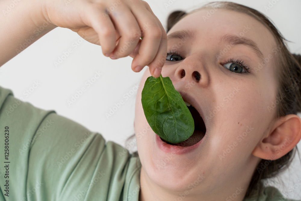 Wall mural Little girl eating spinach. Concept of healthy food and vitamins. Selected focus. Close-up.