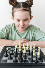Cute little girl sitting in front of a chessboard with a cunning look. Selected focus.