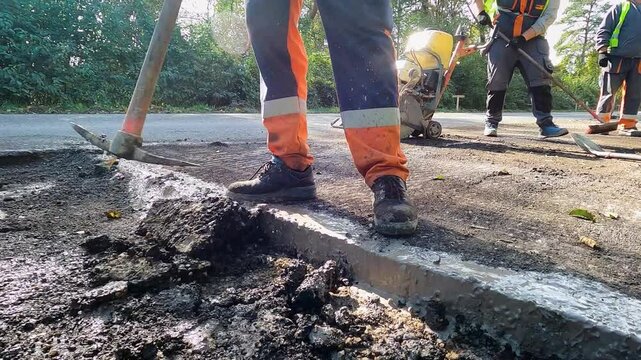 Close-Up of Construction Worker Using a Pick to Remove Old Asphalt at a Road Renovation Site