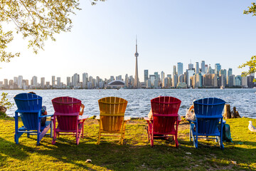 Colorful adirondack chairs on Toronto Island Park at sunset time. Toronto City downtown skyline in...