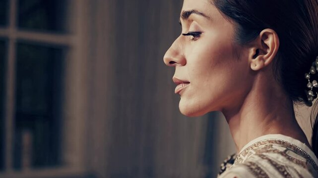 Close-up video portrait of a serene woman with soft lighting and a neutral background, captured from a side angle, highlighting her calm expression.