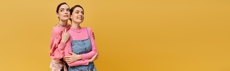 Beautiful twins embracing each other against a vibrant yellow background