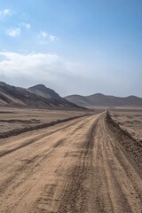Fototapeta premium A dirt road cuts through a barren desert landscape. The road is unpaved with visible tracks from passing vehicles.