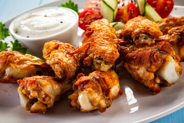 Baked chicken wings with white dressing and fresh salad on wooden table	