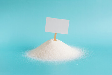 A large amount of granulated sugar and an empty plaque stuck in it in close-up on a light background